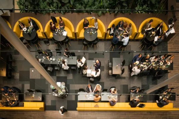 Overzicht van een modern zakelijk restaurant aan de Prinses Beatrixlaan met mensen die lunchen en vergaderen aan ronde en rechthoekige tafels.